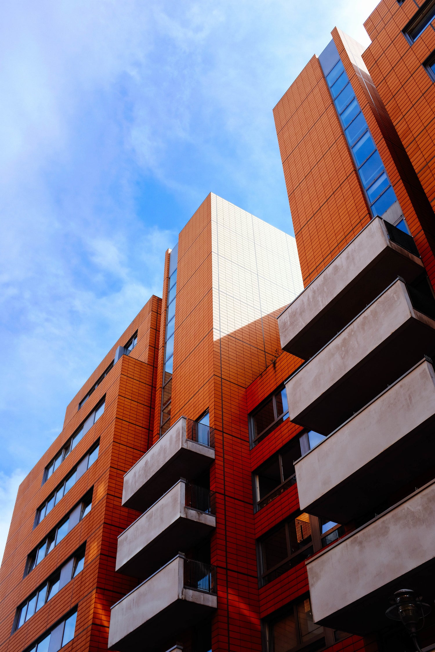 The front of a starkly lit red brick and glass fronted building on a mostly clear day
